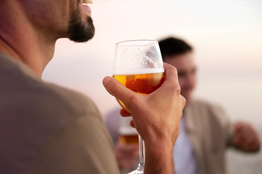 Mann hält ein Glas Bier bei einem Treffen im Freien steht bildlich für Sortimentsentscheidungen und andere Themen im Supply Chain Management
