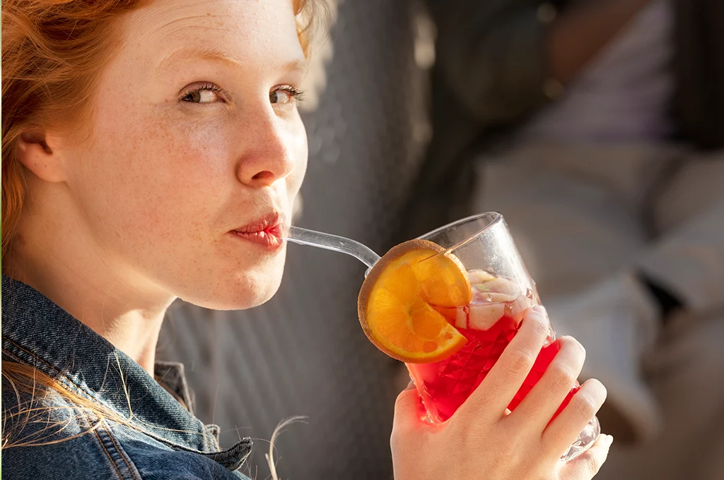 Erfrischungsgetränk mit Orangenscheibe in der Hand einer jungen Frau